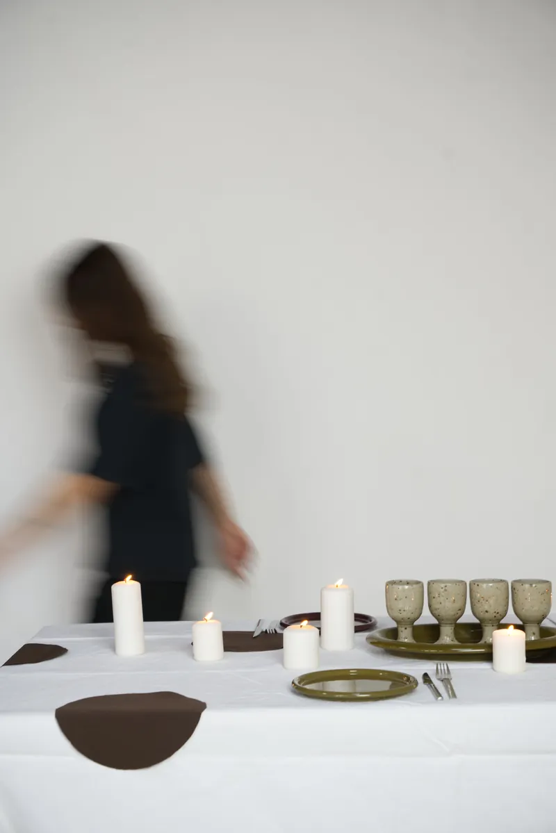 Mise en scène OPA : table dressée de bougies et de verres en céramique, silhouette en mouvement